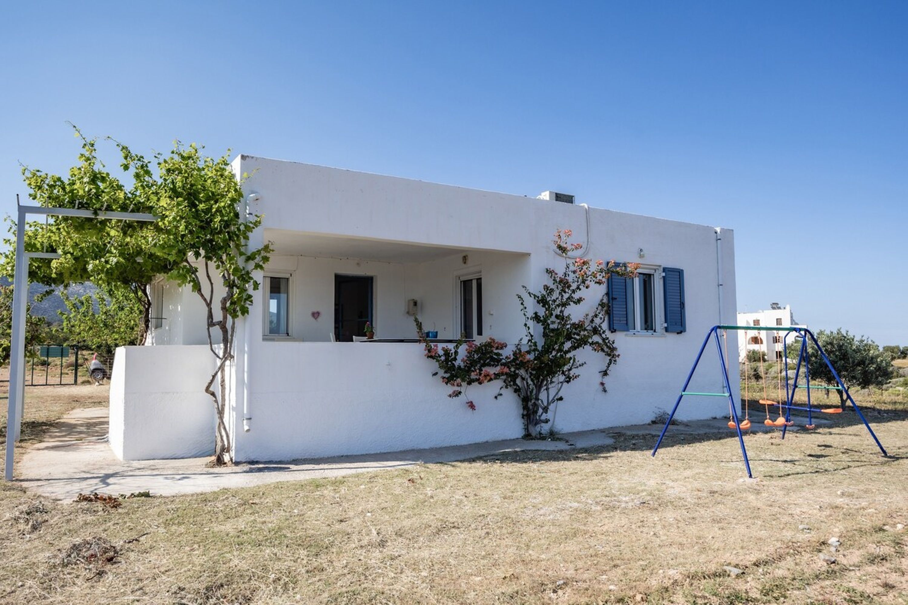 A white building with a small porch, a swing set, and a tree.