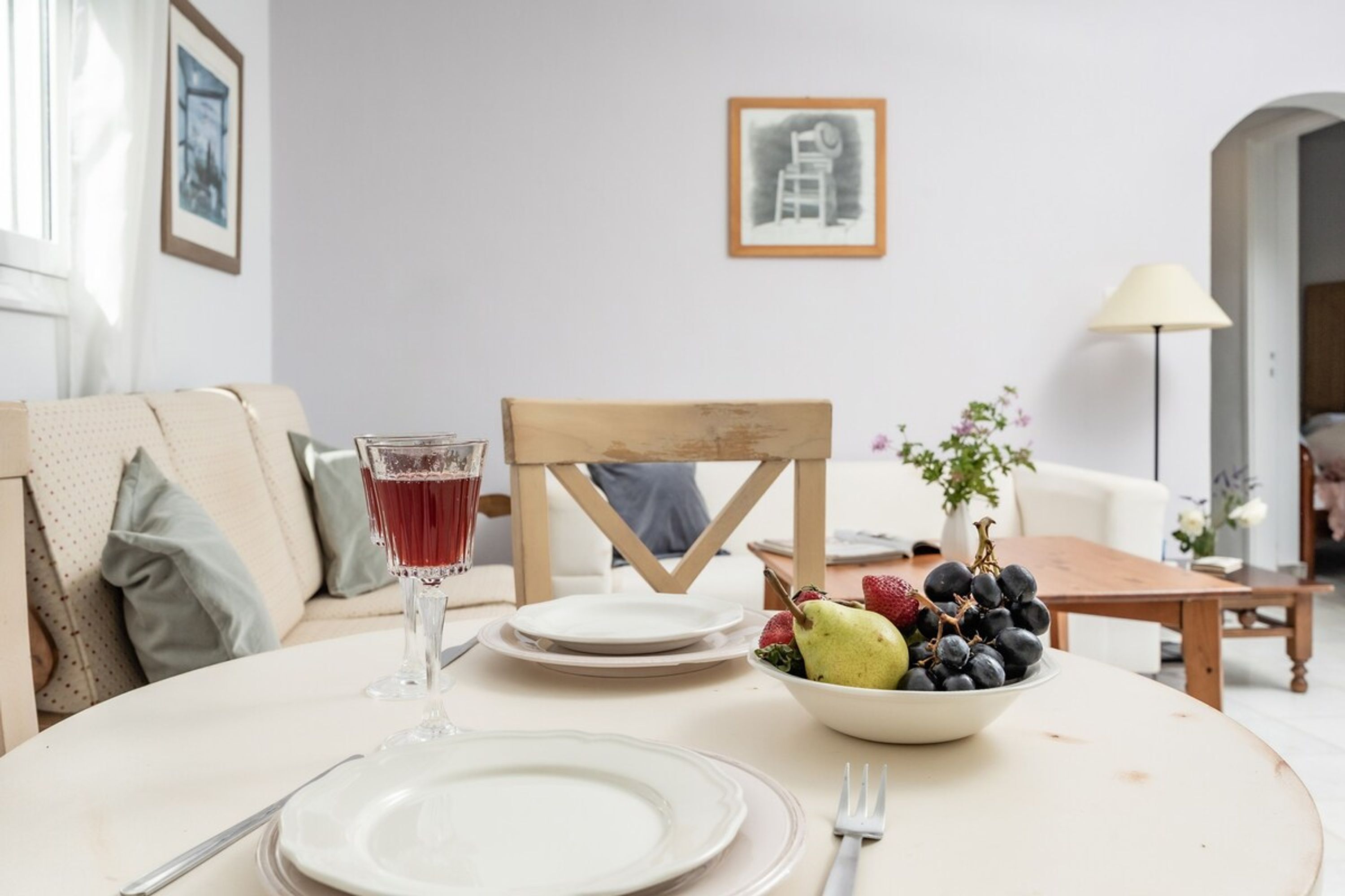 Une table à manger dressée avec des assiettes, un verre contenant une boisson rouge et un saladier rempli de fruits.