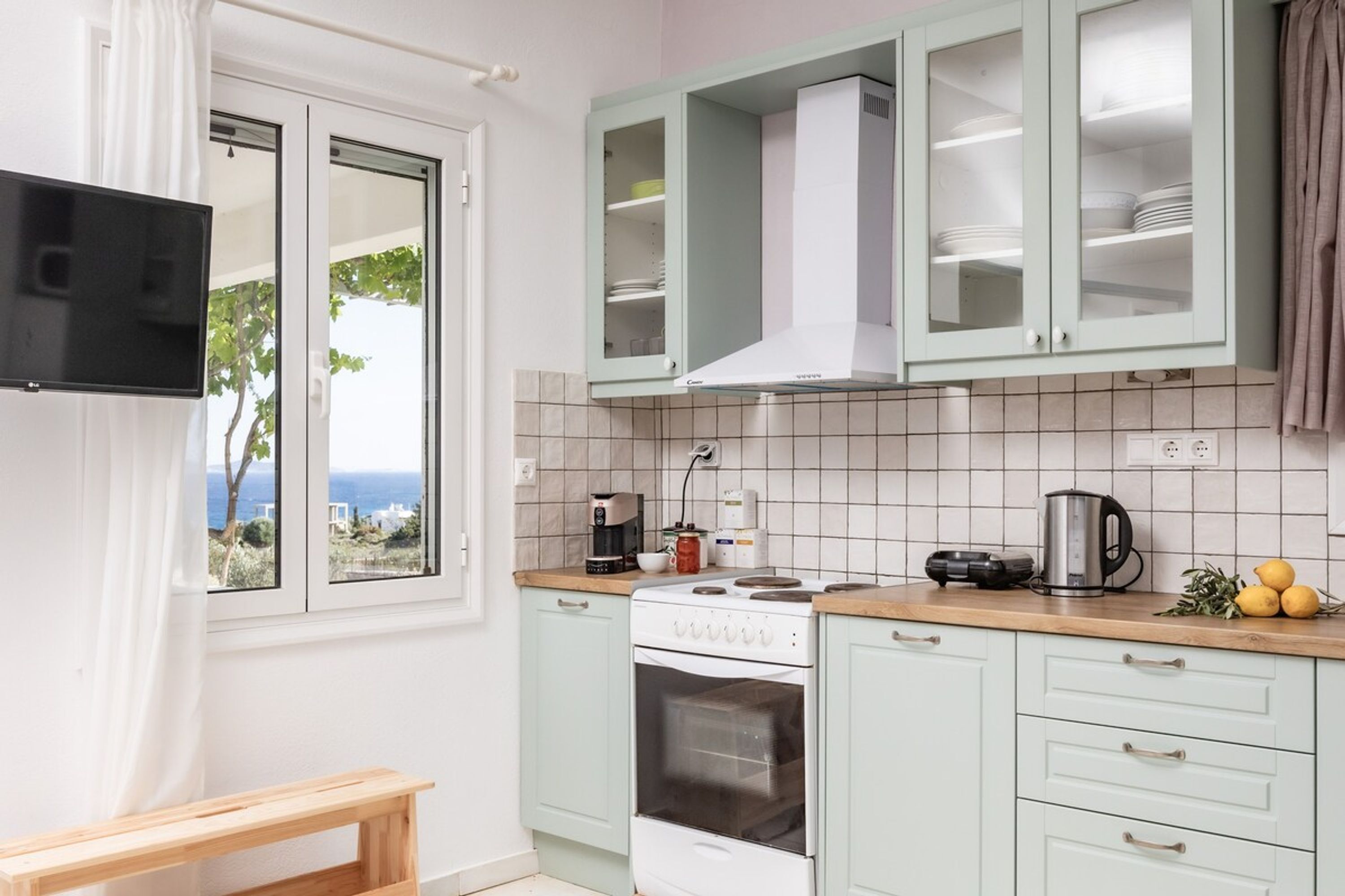 A kitchen with a stove, oven, and cabinets, a window with a view, and a wooden bench.