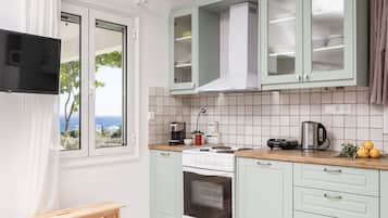 A kitchen with a stove, oven, and cabinets, a window with a view, and a wooden bench.