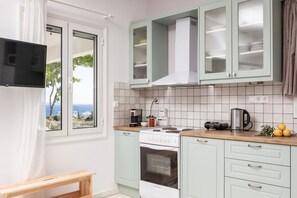 A kitchen with a stove, oven, and cabinets, a window with curtains, and a view of the outdoors.