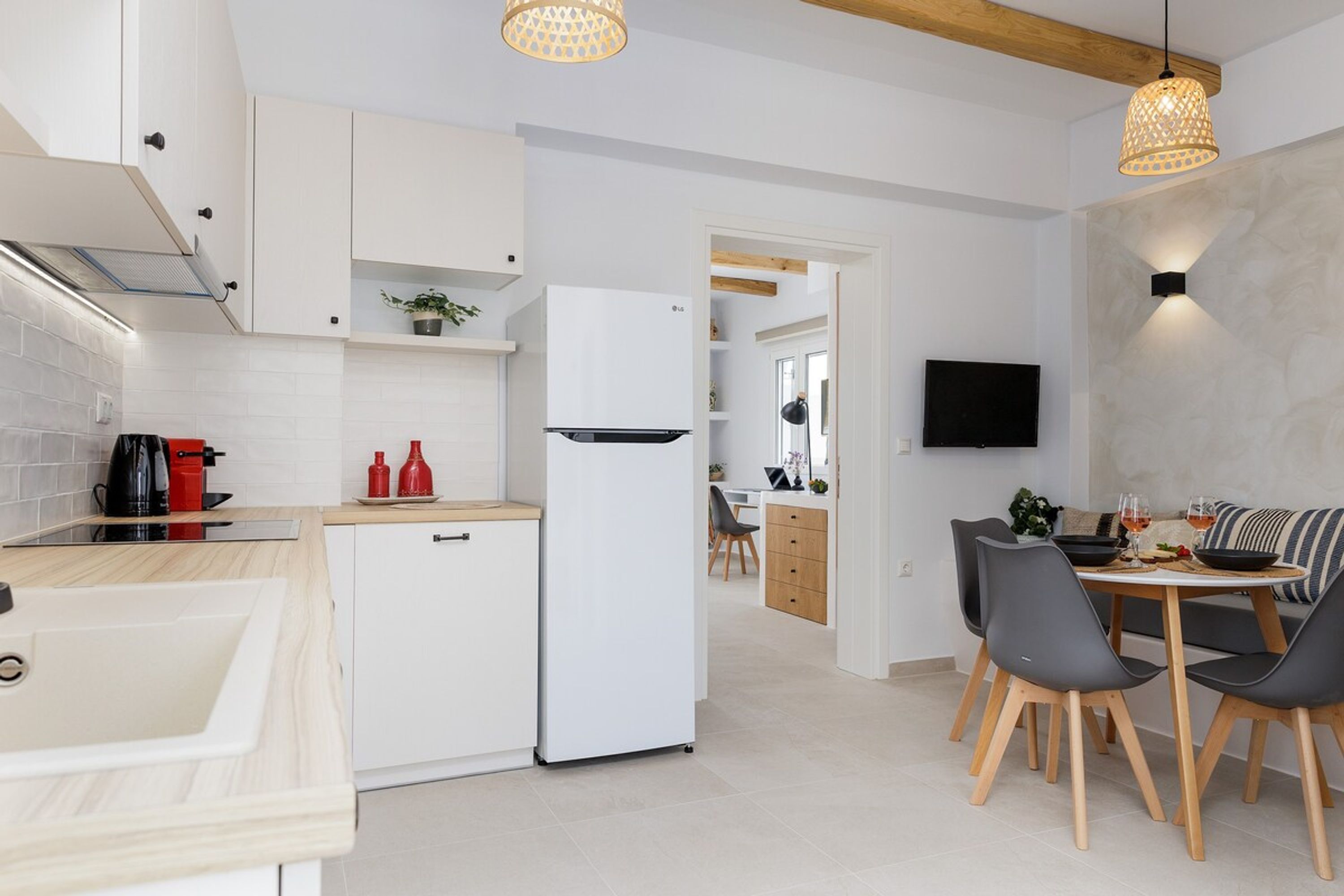 Een moderne keuken met witte kastjes, een ingebouwde oven en een eethoek met een ronde tafel en stoelen.