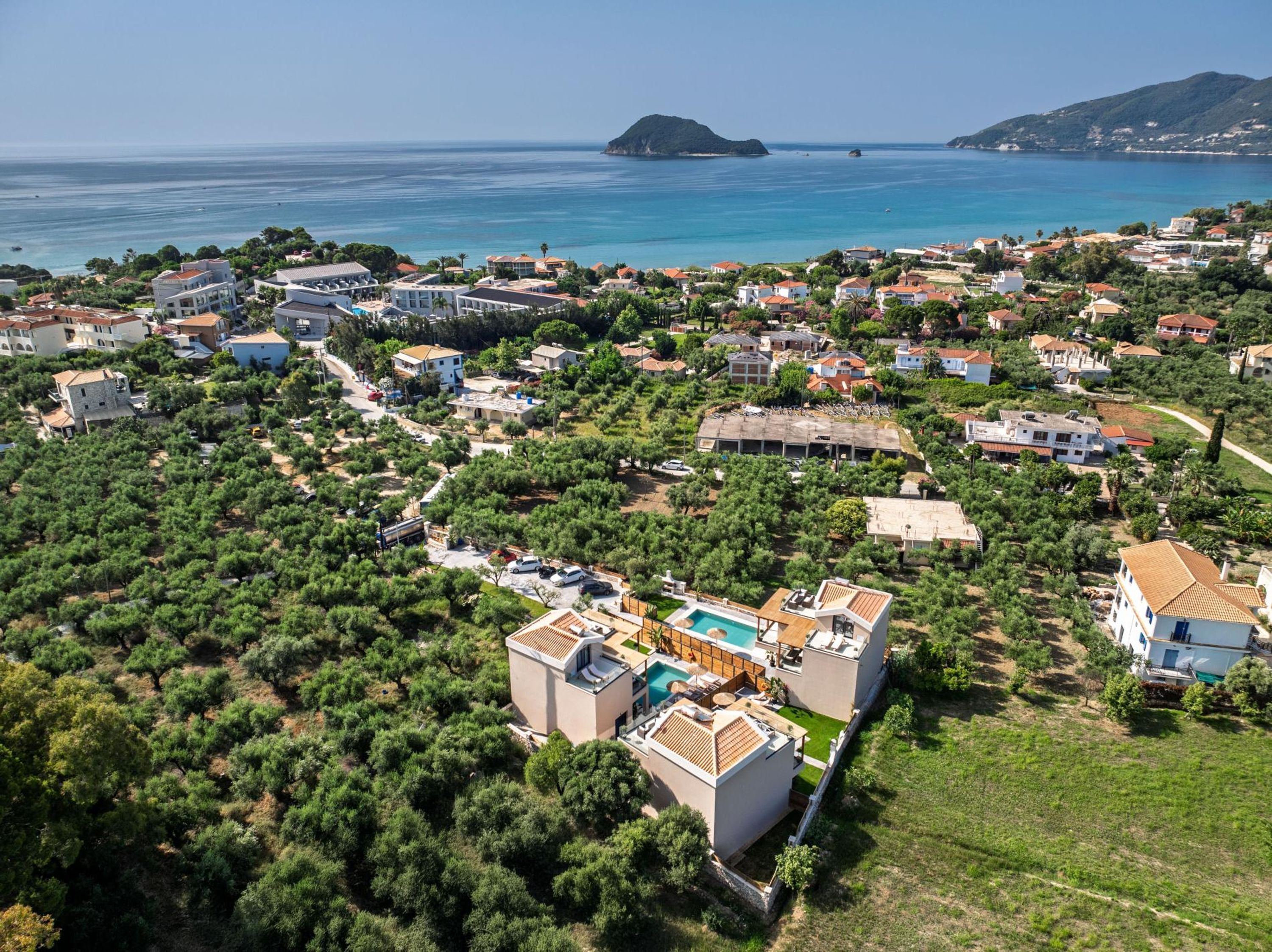 Vue aérienne d’un quartier résidentiel situé sur la côte, avec des maisons, une piscine et une vue sur la mer.