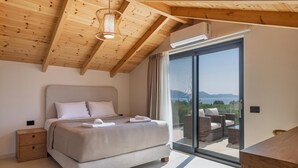 Un dormitorio con una cama grande, una mesita de noche, techo de madera y vistas al exterior a través de una puerta corrediza de vidrio.