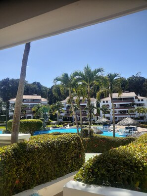 Et resort med swimmingpool, palmer og en høj bygning med altaner.