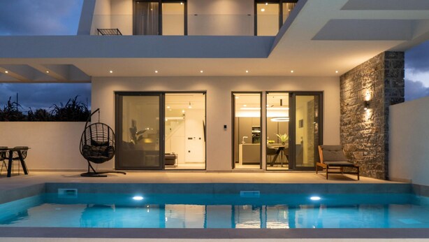 Ein modernes, zweistöckiges Haus mit Pool, großen Schiebeglasfenstern und einer Außenwand aus Naturstein.