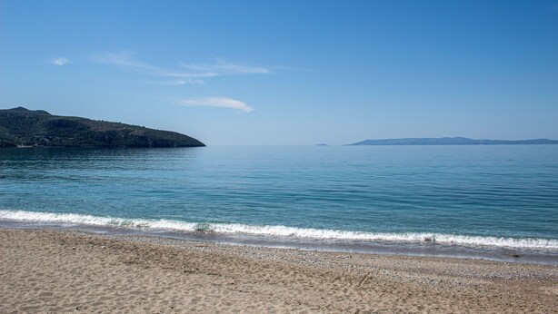 Una spiaggia con acque cristalline, una costa sabbiosa e colline in lontananza.