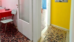 Una stanza con un tavolo rosso, una sedia decorata, una porta con un pannello in vetro satinato e un muro giallo con un quadro incorniciato.