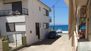 Una stretta via con un edificio sul lato sinistro e vista sul mare a destra. Due auto parcheggiate lungo la strada.