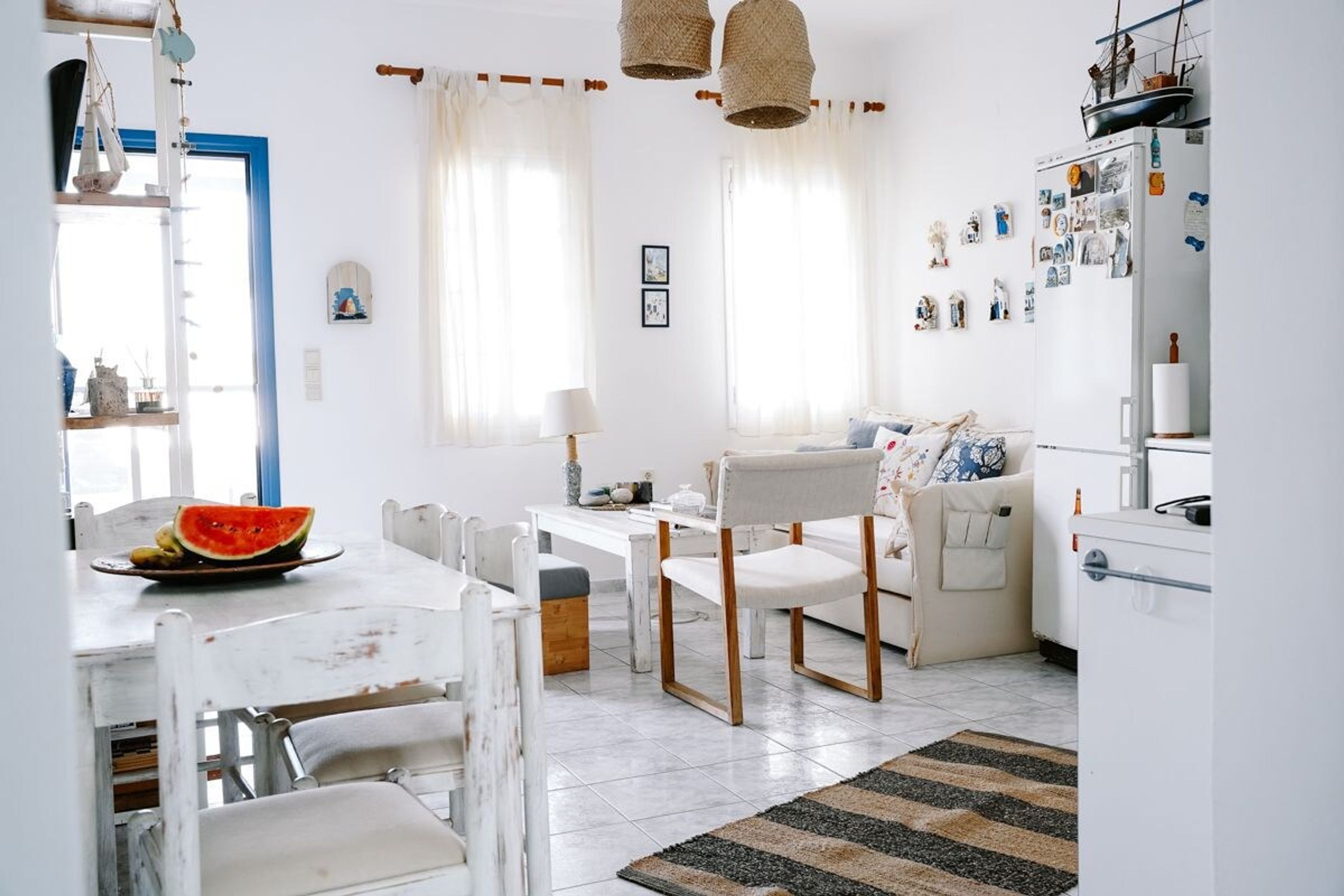 A bright, well-lit kitchen with white cabinetry, a dining table with chairs, and a refrigerator with magnets and pictures.