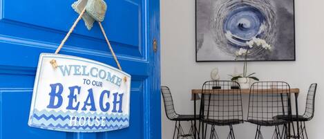 A blue door with a 'Welcome to our Beach House' sign and a dining area with a table and chairs.