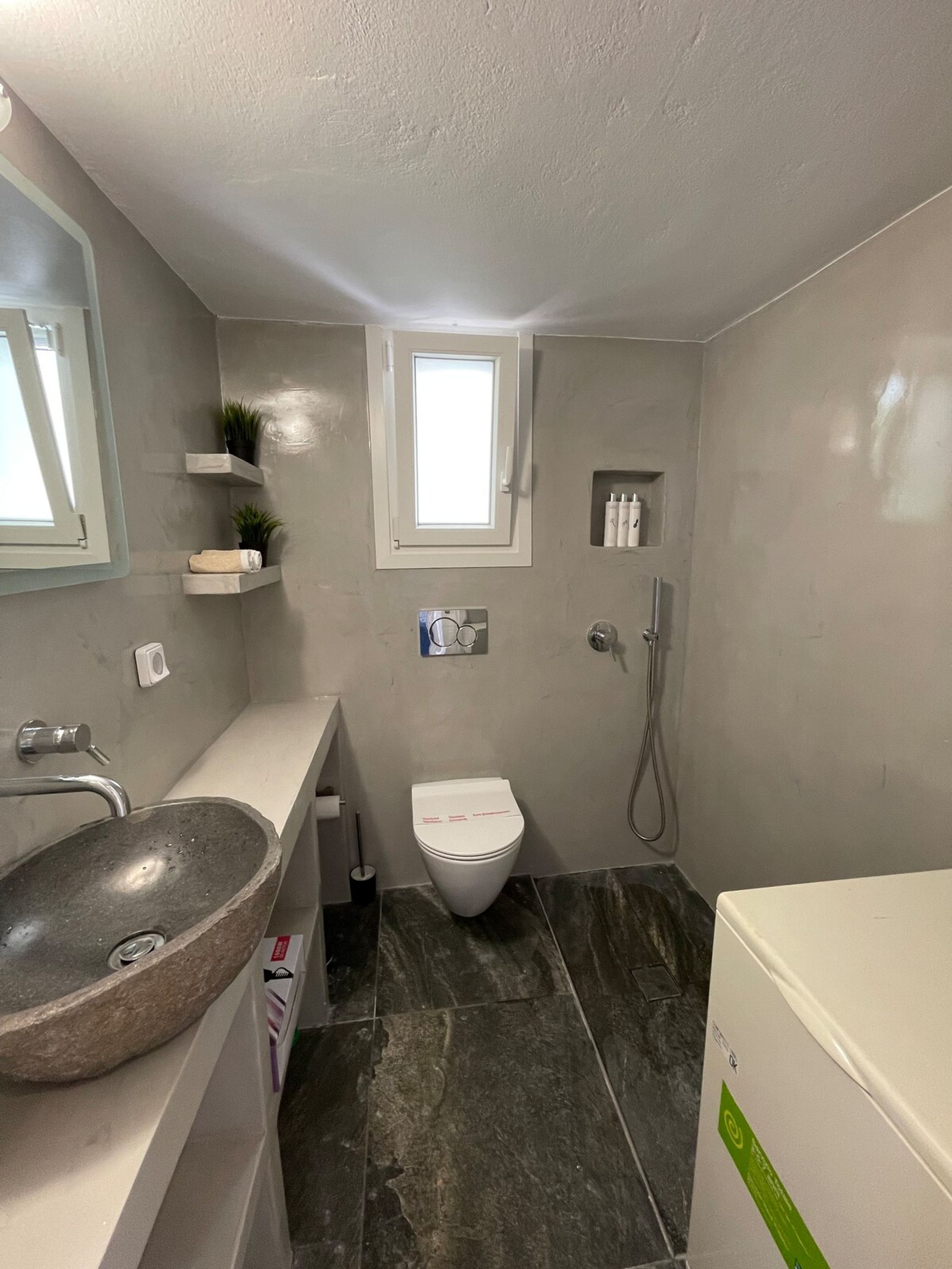 A bathroom with a stone sink, a toilet, a shower, and a small window.