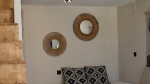 Ein gemütliches Wohnzimmer mit einer Holztreppe, einem runden Tisch mit einer Kerze, einem gemusterten Kissen und zwei Wandspiegeln.