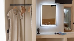 Une salle de bain avec un miroir, un porte-serviettes avec des vêtements, une chaise en bois et une étagère avec des articles de toilette.