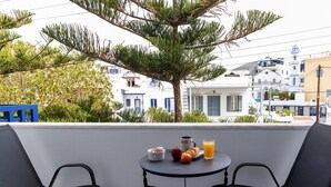 Un balcon avec une table préparée pour le petit-déjeuner, comprenant un bol, une pomme, une orange, un croissant et un verre de jus d’orange.
