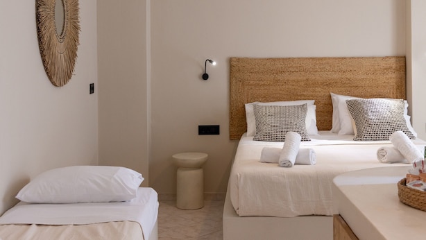 Une chambre d’hôtel avec deux lits, une tête de lit en osier, une petite table ronde et un luminaire fixé au mur.