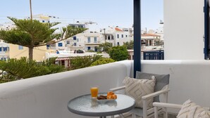 A balcony with a round table, two chairs, a glass of orange juice, and a plate with oranges. - Salt & Stone In Center Of Tinos Luxury Suite (Tinos)