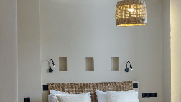 A hotel room with a bed, bedside table, mirror, and a hanging light fixture. - Salt & Stone In Center Of Tinos Luxury Suite (Tinos)