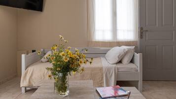 Ein Schlafzimmer mit einem Bett, einem Nachttisch mit Blumenvase und einem Fenster mit transparenten Vorhängen.
