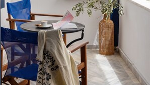 Een balkon met een tafel, stoelen, een rieten vaas en een uitzicht op witte gebouwen met blauwe accenten.