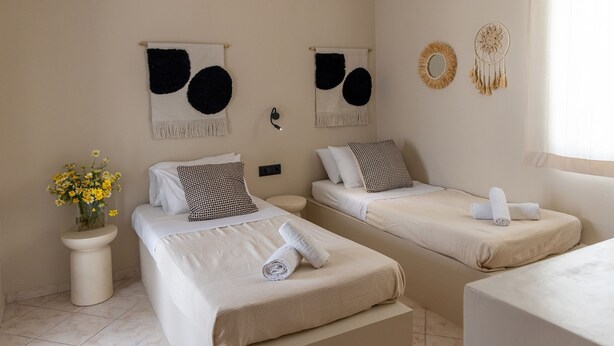 A hotel room with two beds, a bedside table with a vase of flowers, and wall decorations including dream catchers. - Atheria In Center Of Tinos With Two Single Beds (Tinos)