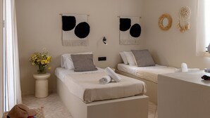 A hotel room with two beds, a small bedside table with a vase of flowers, and wall decor including dreamcatchers. - Atheria In Center Of Tinos With Two Single Beds (Tinos)