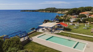 Un espace piscine avec vue sur la mer, des sièges extérieurs et un patio couvert.