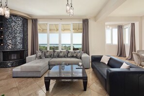 A spacious living room with a large sectional sofa, a glass coffee table, and a view of the sea through large windows. - Villa Mediterranean View (Corfu)