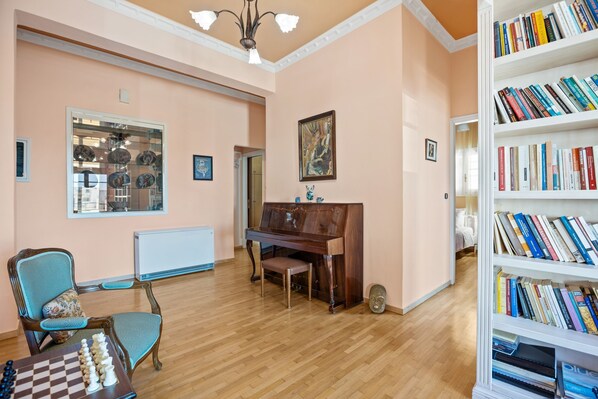 A room with a wooden floor, a piano, a bookshelf, and a chessboard. - Artistic Apartment in Chania (Chania)