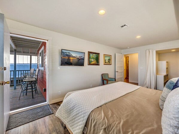 A bedroom with a large bed, a chair, a desk, and a view of the outdoors.