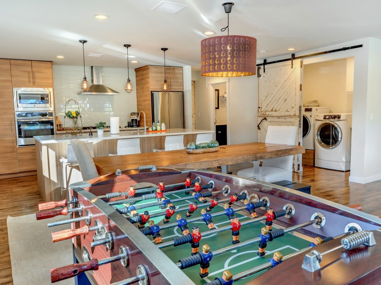 A modern kitchen with a foosball table, a dining area, and a laundry room.
