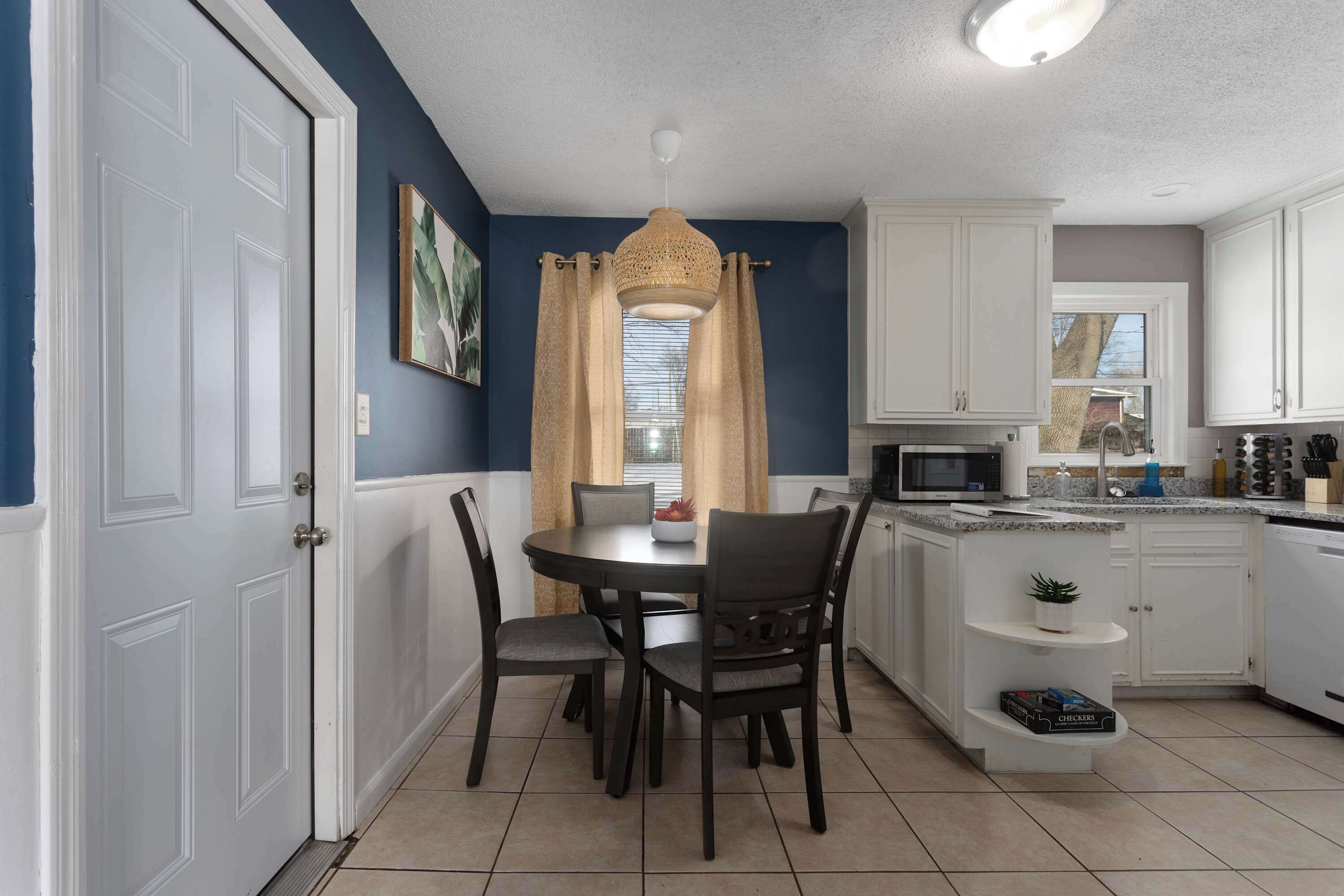 A compact kitchen with white cabinets, a dining table with chairs, a microwave, and a sink.