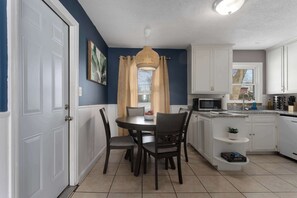 Une cuisine compacte avec des meubles blancs, une table à manger avec des chaises, un four à micro-ondes et un évier.