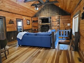 A log cabin interior with a blue sofa, a fireplace, and a staircase. - Moonlight Creek Cabin, 3 miles to downtown, luxury cabin, sleeps 10 (Blue Ridge)