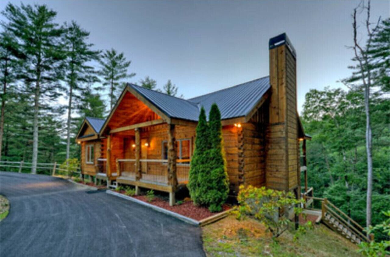 A log cabin with a porch, surrounded by forest.