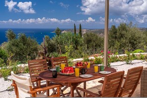 A round wooden table set outdoors with chairs, a bowl of fruit, and drinks. - Villa Onera in Vlachata (Vlachata)