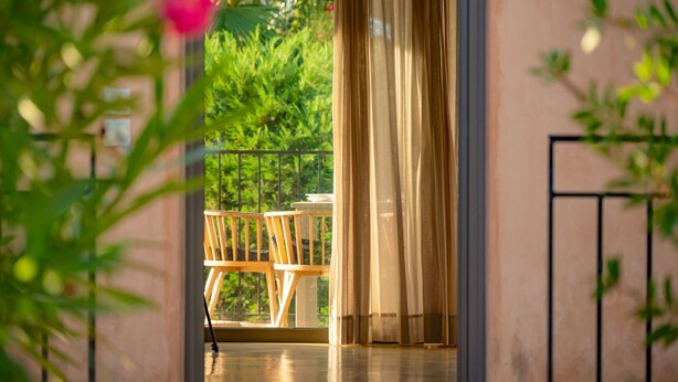 Um espaço interior com vista para o verde lá fora, uma cadeira de madeira e uma mesa.