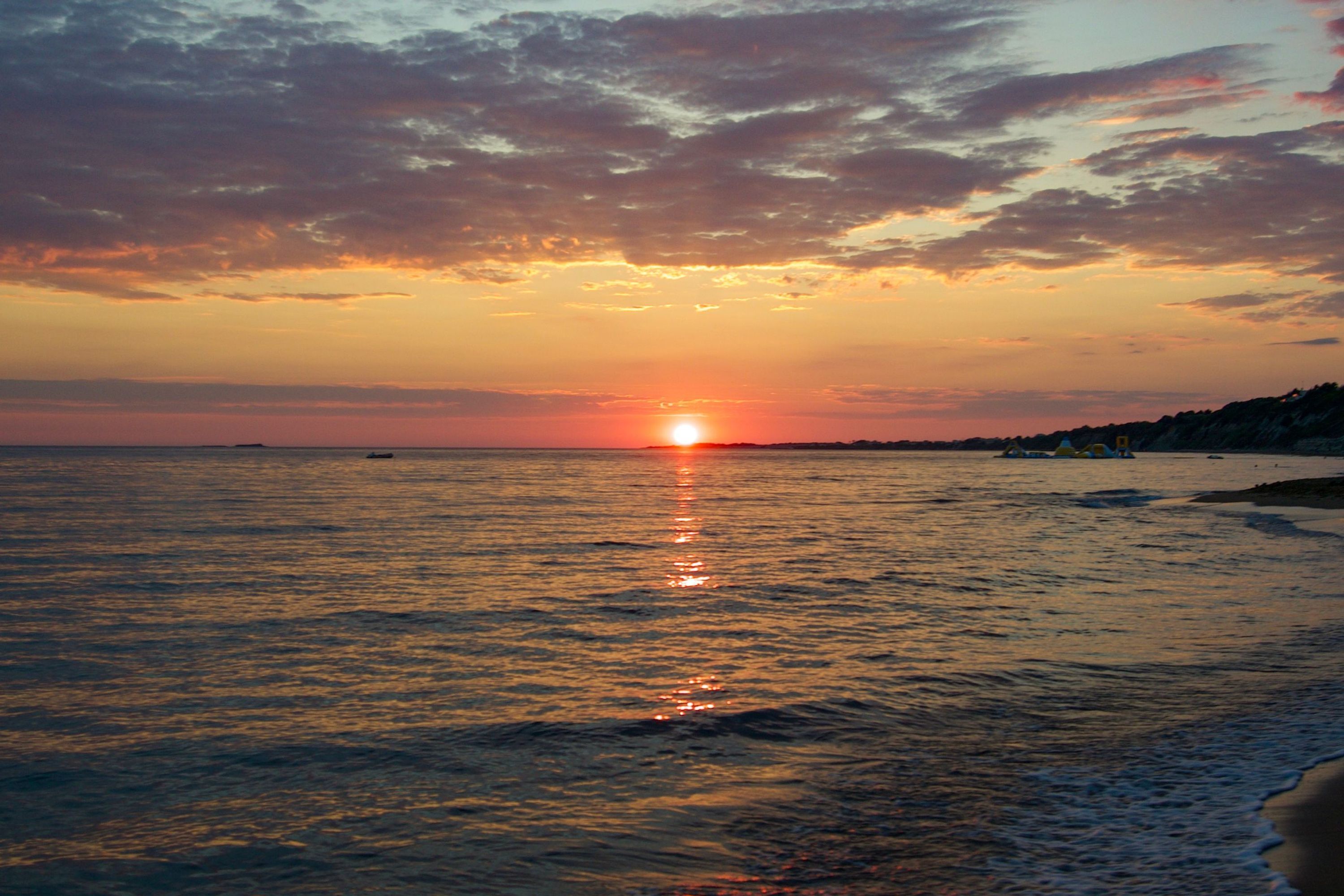 Ein Sonnenuntergang über ruhiger See, mit einem Strand auf der rechten Seite.