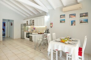 Eine moderne Küche mit weißen Schränken, eine Essecke mit einem weißen Tisch für vier Personen und ein Flur, der in ein weiteres Zimmer führt.