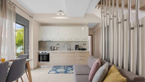 A modern kitchen with white cabinets, a dining area with a table and chairs, and a living area with a sofa and cushions. - Park and sea view Villa with Private Pool 2 (Chania)