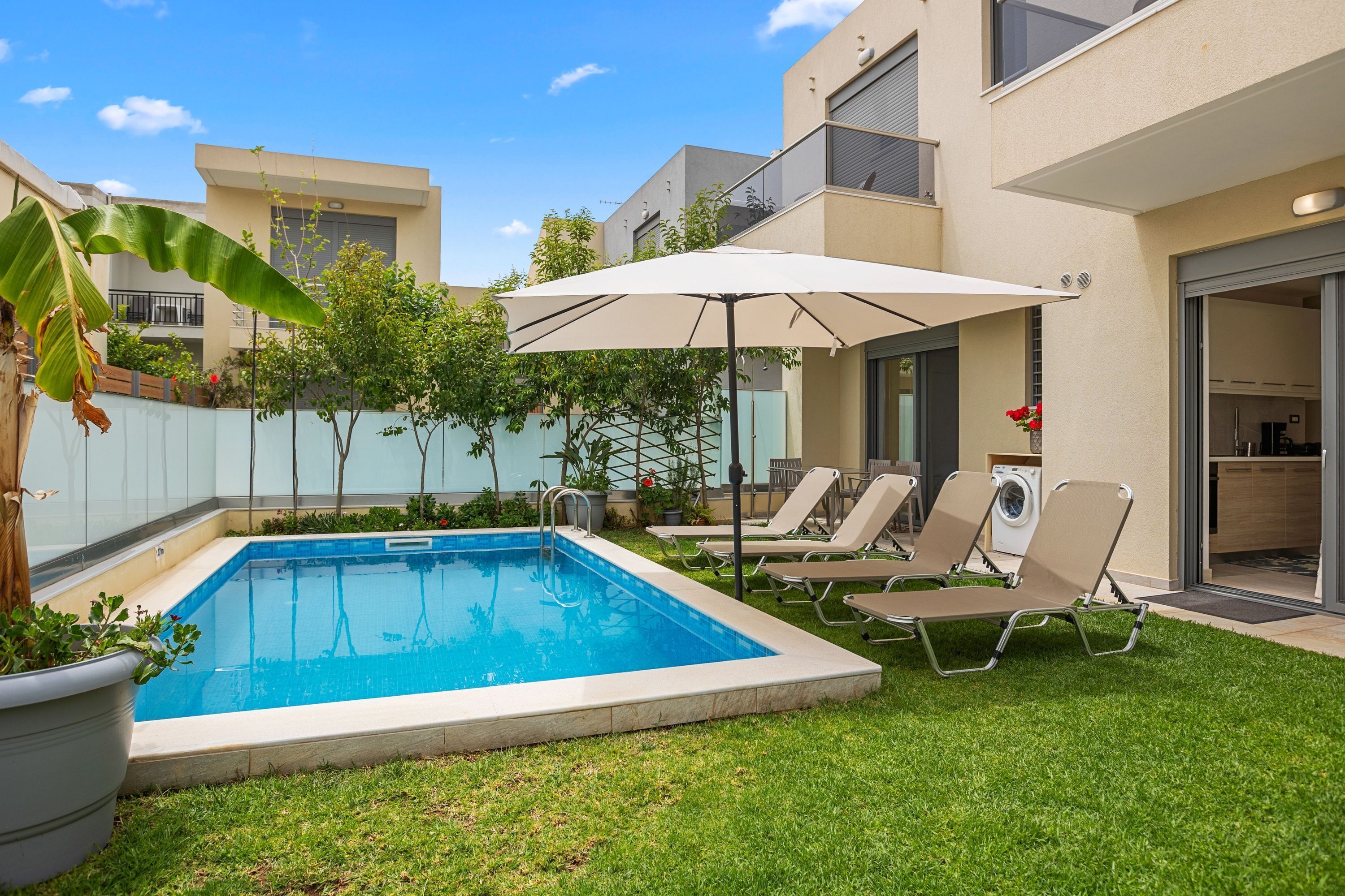Ein moderner Poolbereich im Freien mit einem kühlen, blauen Pool, einem großen Sonnenschirm und zwei Liegestühlen.