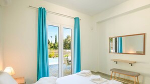 Ett hotellrum med en säng, en bänk, en spegel och utsikt över ett utomhusområde med en pool och grönska.