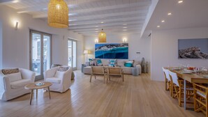 Amplia sala de estar con piso de madera, sofás blancos y una mesa de comedor preparada para seis personas.
