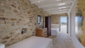 Un dormitorio con paredes de piedra, un aparador de madera, una cama y vistas al exterior.