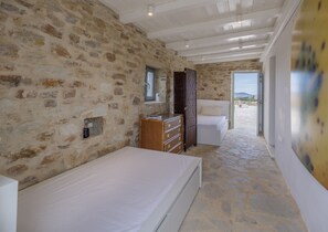 Ein Schlafzimmer mit Stehwänden, einer Holzkommode, einem Bett und Blick ins Freie.