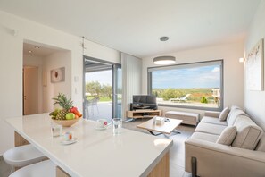 A modern living room with a sofa, a coffee table, and a TV. There is a fruit bowl on the counter and a window with a view of the outdoors. - Sunset Villa in Moudania (Moudania)