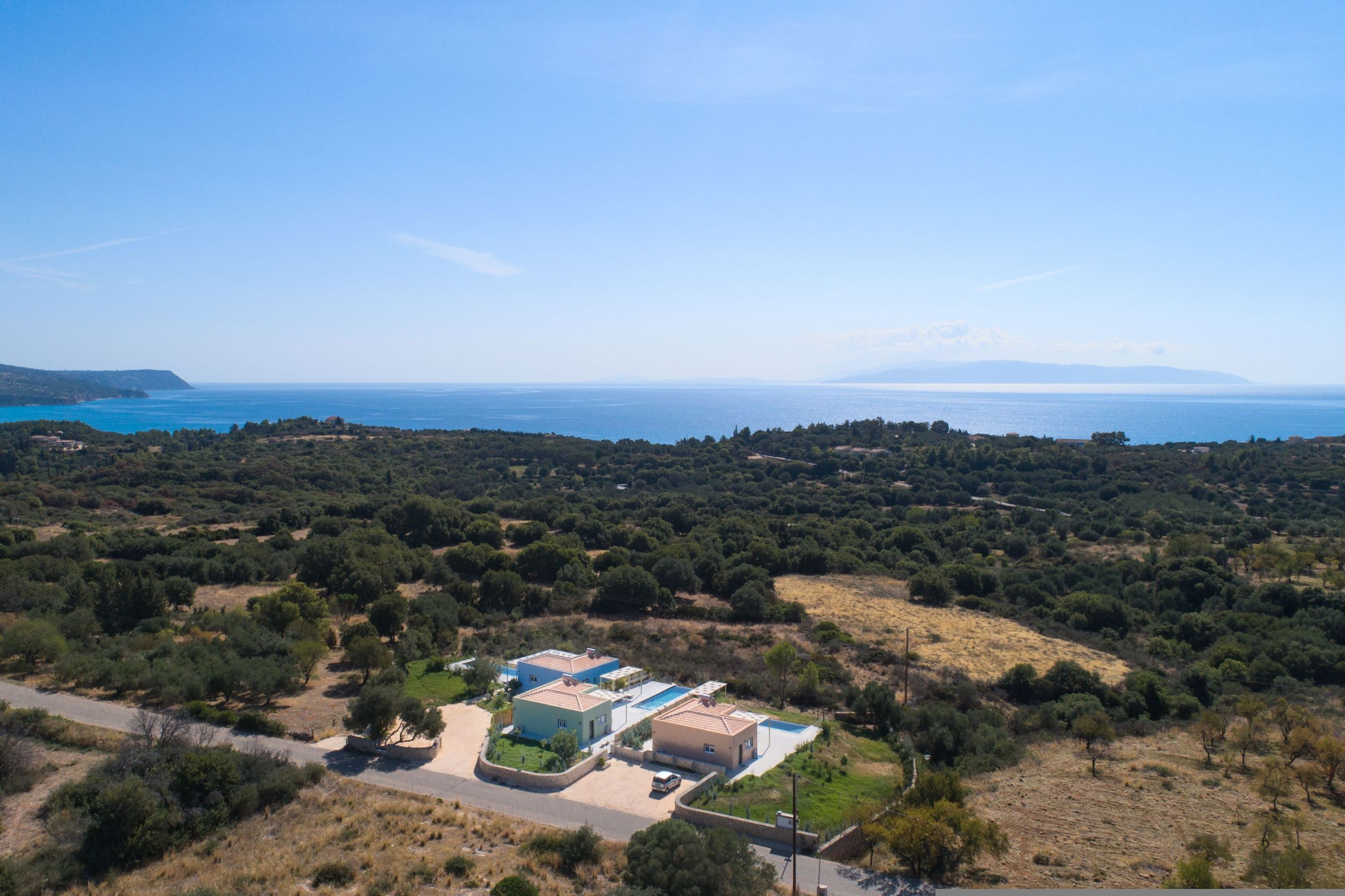 An aerial view of a coastal property with multiple buildings, a road, and surrounding vegetation.