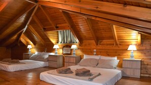 A cozy attic bedroom with wooden beams, two beds, bedside lamps, and a window with curtains. - Tsampika's Traditional Stone Cottage in Siana (Siana)