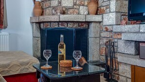 A stone fireplace with a wine bottle and glasses on a glass table. - Tsampika's Traditional Stone Cottage in Siana (Siana)
