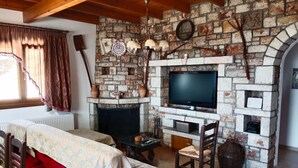 A cozy living room with a stone fireplace, a television, and a comfortable seating area. - Tsampika's Traditional Stone Cottage in Siana (Siana)
